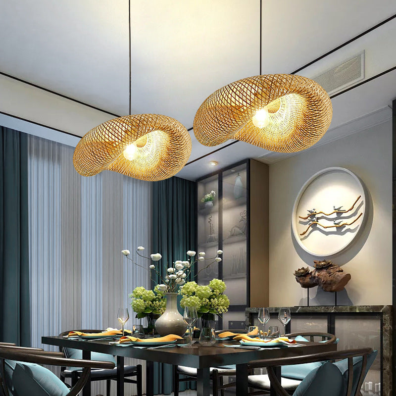 A dining room with a contemporary Southeast Asian style features a table set for a meal, complete with plates, cutlery, and glasses. Two XCEPTION Living Room Ceiling Lights made of bamboo illuminate the space from above. A decorative wall piece and a vase with green flowers add charm to the setting.