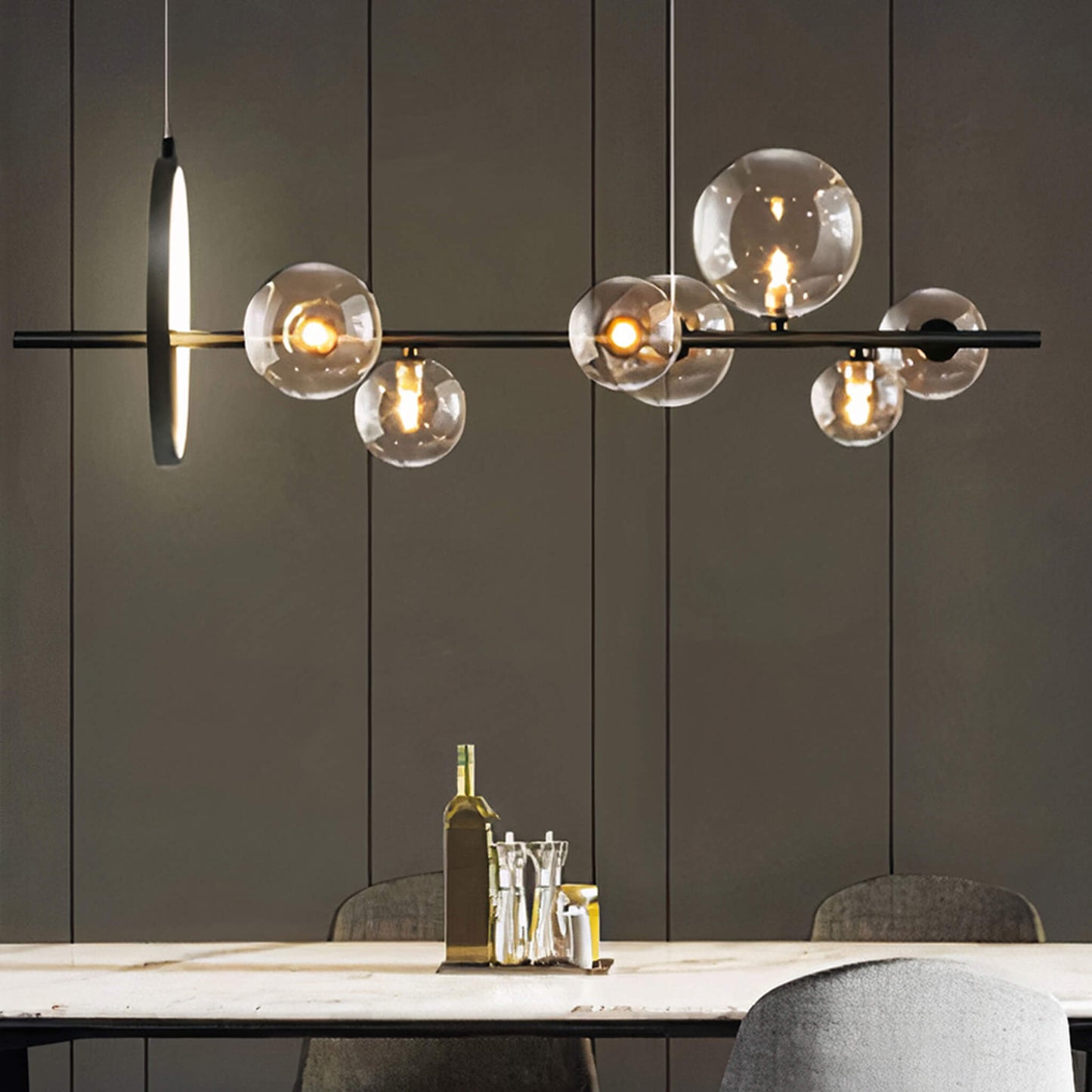 A contemporary dining room showcases the XCEPTION Art Deco Ceiling Lights, featuring elegant spherical glass bulbs. Beneath, a wooden table is elegantly arranged with a bottle, salt and pepper shakers, and two upholstered chairs set against a richly paneled wall.