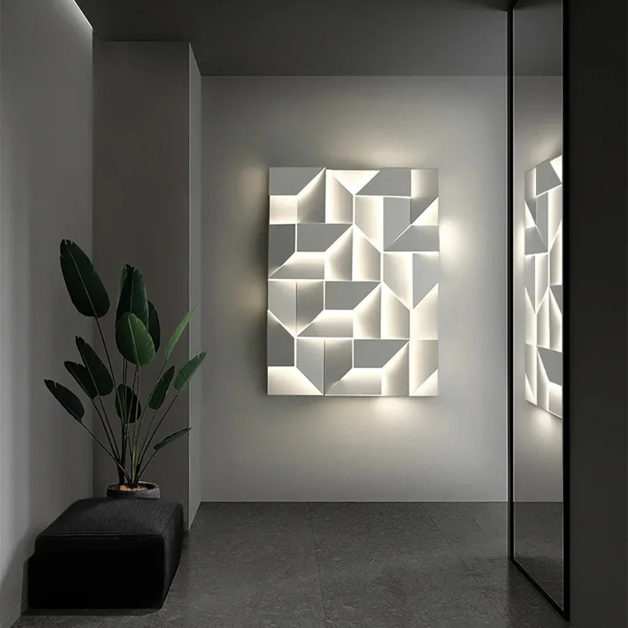 A contemporary room features the XCEPTION Geometric wall lights, creating a stylish art installation that emits a gentle radiance. To the left, a potted plant rests on a dark bench, while on the right, a mirror reflects the artwork. These lights provide adjustable color temperatures for improved ambiance.