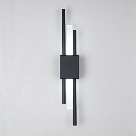 The Glitch Wall Light by XCEPTION is a contemporary wall fixture featuring three vertical rods—two black and one luminous white—that encase a central black rectangular base, all mounted on a plain white wall.