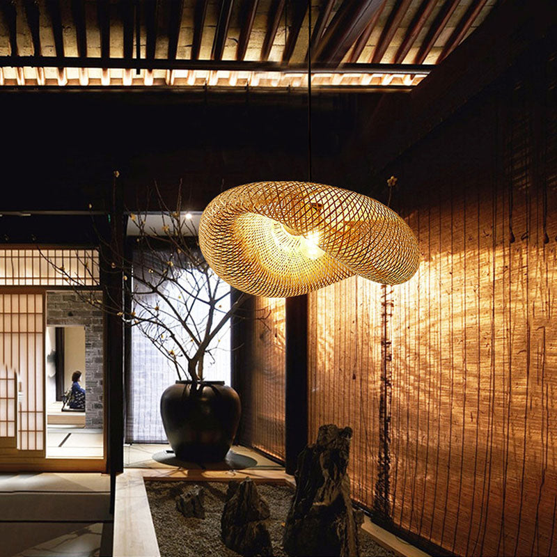 A large, intricately woven Living room ceiling light by XCEPTION adds a captivating charm to the dimly lit room, casting patterned shadows. The space is beautifully accented with a potted tree, stones scattered across the floor, and sliding doors, all of which contribute to creating a serene Southeast Asian-style atmosphere enhanced by an ambient LED light glow.