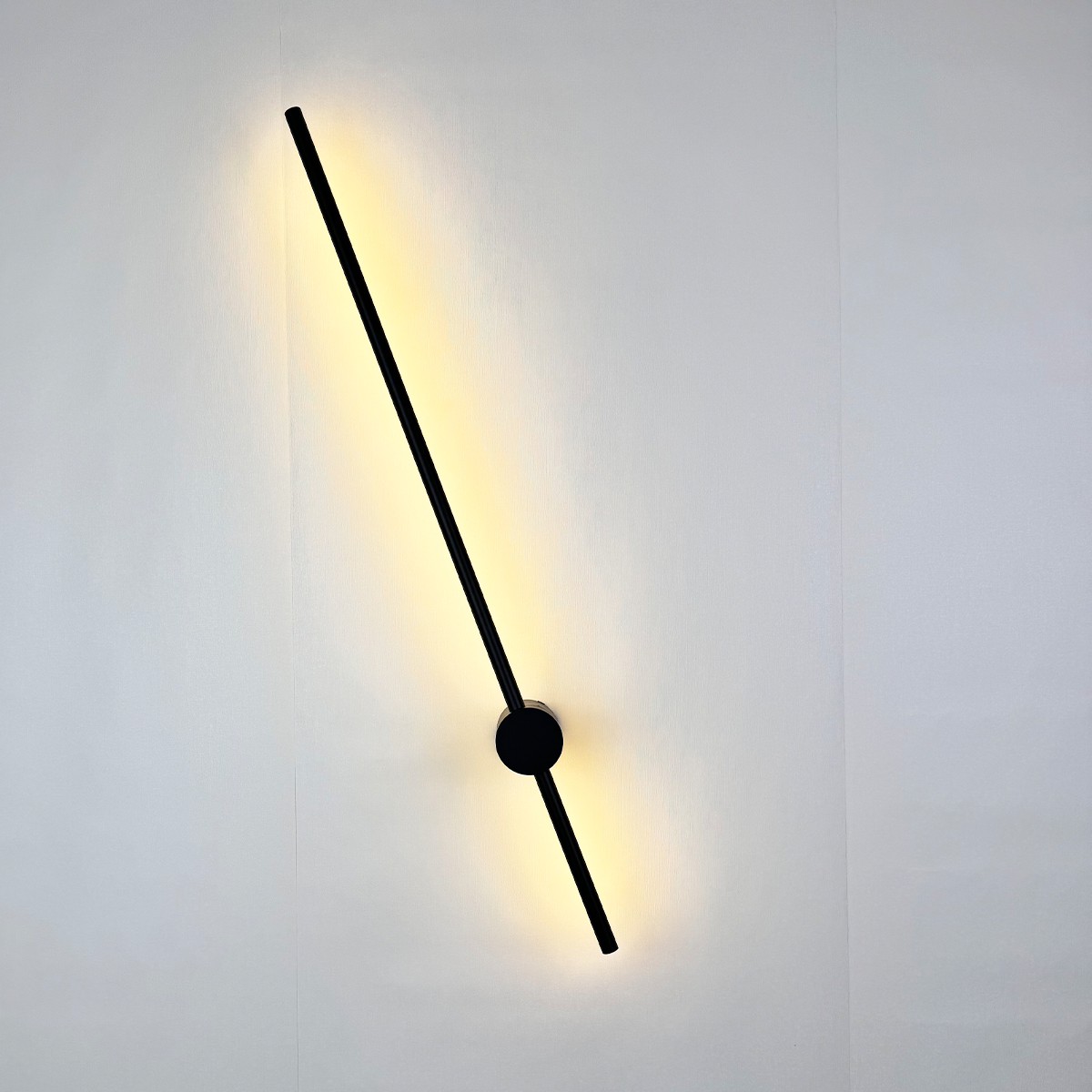 The Nordic Light Stick • 2-Pack by XCEPTION features a sleek, black diagonal line design that emits a soft yellow glow. Mounted on a white wall, these modern wall lamps create a warm and minimalist ambiance.