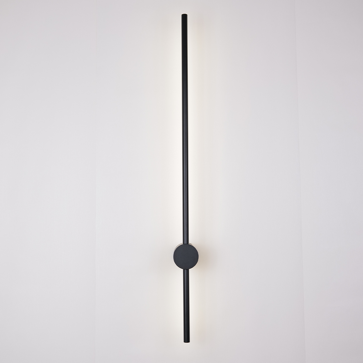 Introducing the Nordic Light Stick • 2-Pack by XCEPTION: a contemporary minimalist wall light design that showcases a vertical black rod mounted on a circular base. This elegant rod casts a gentle, even glow across the plain, off-white surface behind it.
