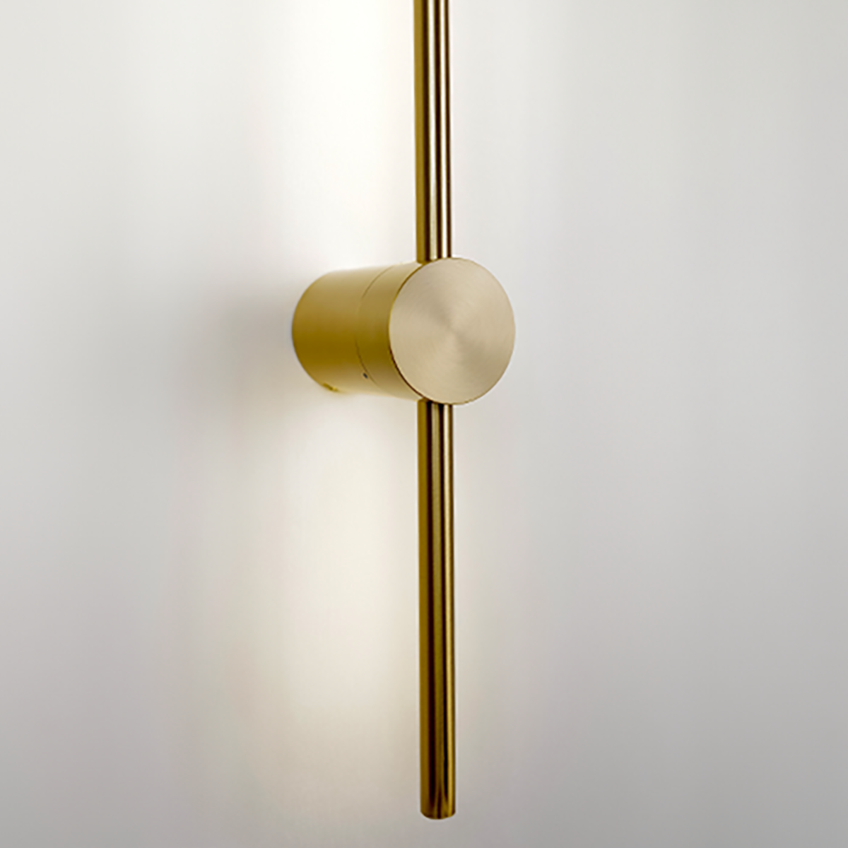 The Nordic Light Stick • 2-Pack by XCEPTION is a modern, minimalist brass door handle featuring a vertical cylindrical design mounted on a white surface. The polished metal reflects light, offering a sleek and elegant appearance.