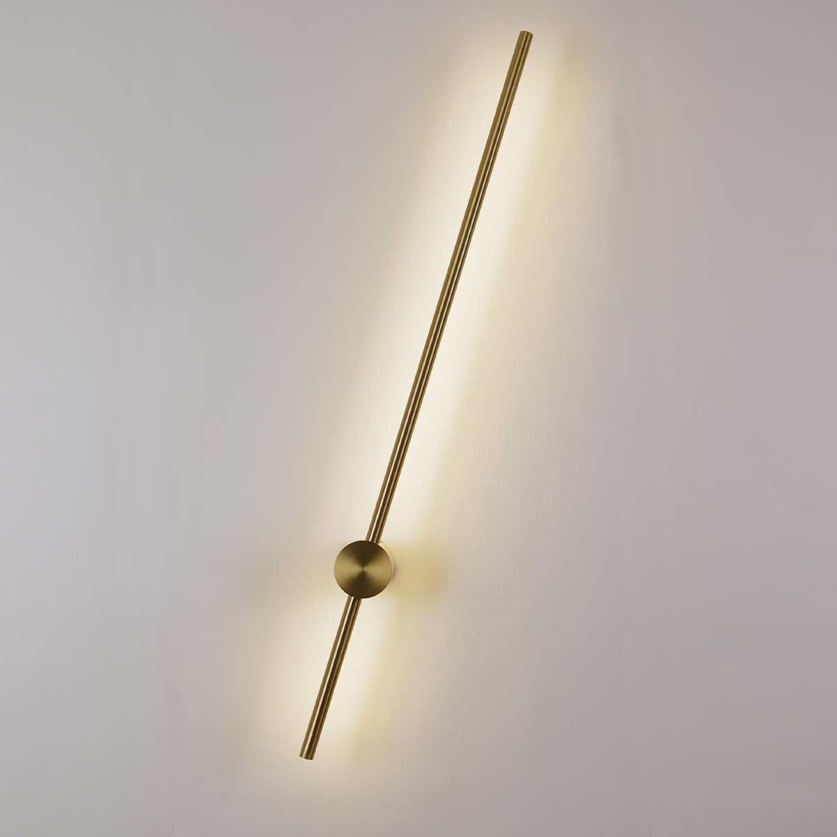 The Nordic Light Stick • 2-Pack by XCEPTION features a minimalist design with long, slender brass rods that emit a warm glow against a white wall. Each rod is diagonally positioned with a circular mount at its center.