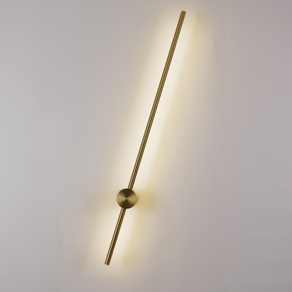 The Nordic Light Stick • 2-Pack by XCEPTION features a minimalist design with long, slender brass rods that emit a warm glow against a white wall. Each rod is diagonally positioned with a circular mount at its center.