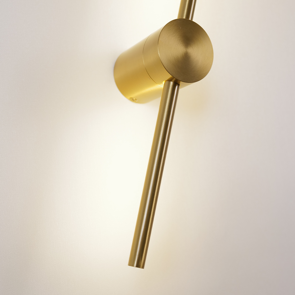 The Nordic Light Stick • 2-Pack by XCEPTION offers a sleek, modern wall-mounted design featuring a gold cylindrical shape. It emits soft light against a white wall, enhancing the minimalist aesthetic.
