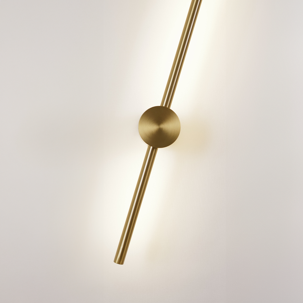 Presenting the XCEPTION Nordic Light Stick • 2-Pack, this modern and minimalist wall light features a gold cylindrical rod and circular center mount. The rod's angled design emits a soft, warm glow, elegantly enhancing its sleek aesthetics against a plain white backdrop.