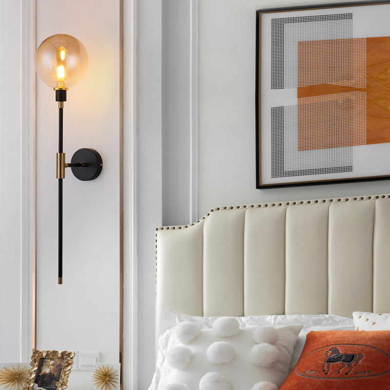 A bedroom corner features the Scandi Wall Lights by XCEPTION, known for their modern design and energy-efficient LED technology. Complemented by a large abstract art piece in orange and black, the space also includes a tufted beige headboard with decorative pillows. A side table holds a framed photo alongside a small decorative sculpture.