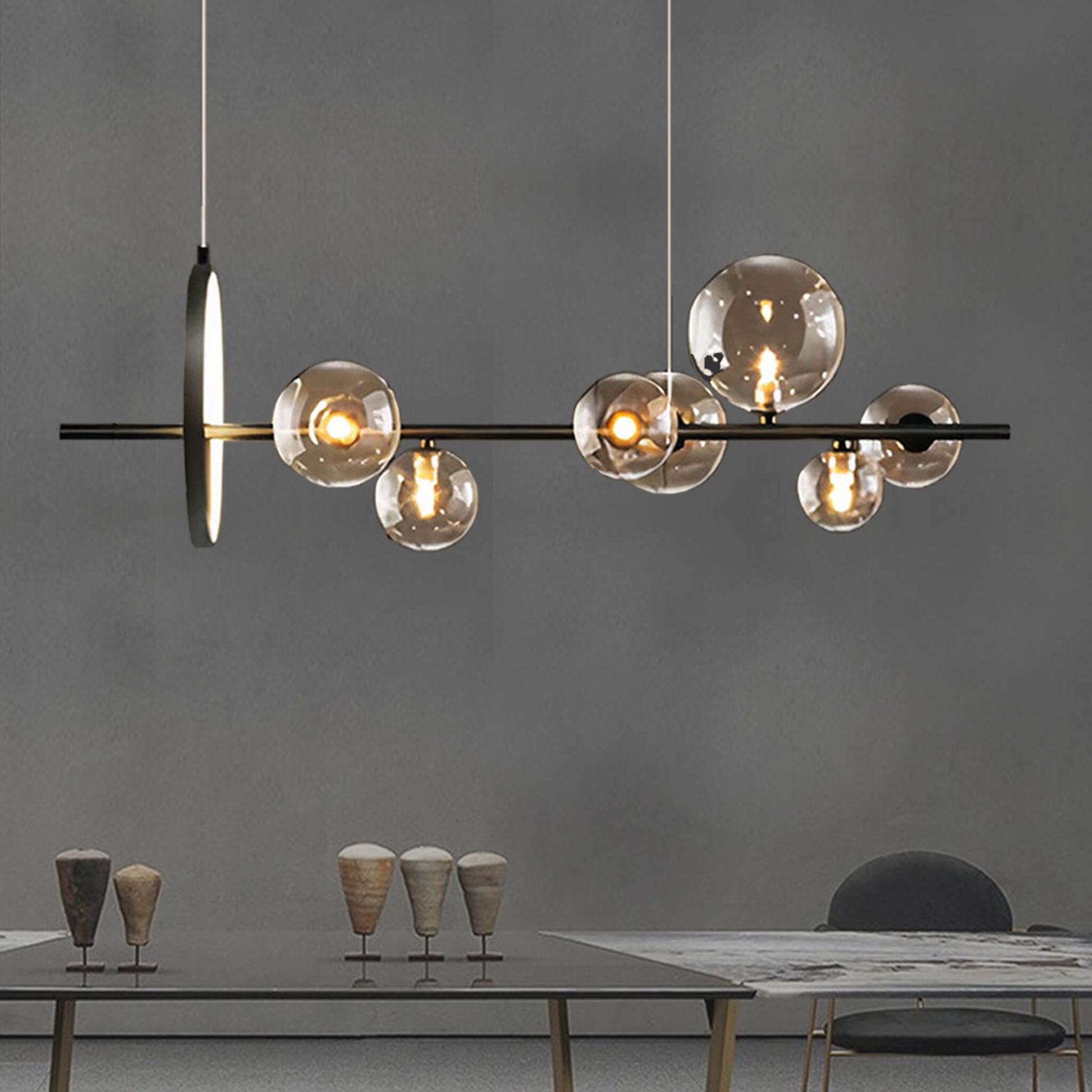 An Art Deco ceiling light from XCEPTION, featuring multiple spherical glass bulbs, is elegantly suspended above a dining table. The table is adorned with several cone-shaped decorative items and a partially visible chair, all set against a plain gray wall.