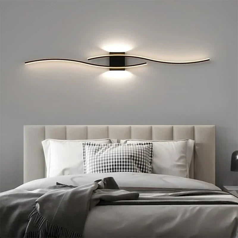 A modern bedroom showcases a light gray upholstered headboard and monochrome bedding with checkered pillows. Above the bed, XCEPTION's Minimalisto Wall Light provides a soft, ambient glow against the gray wall, enhancing the room's contemporary design with its sleek and subtle elegance.