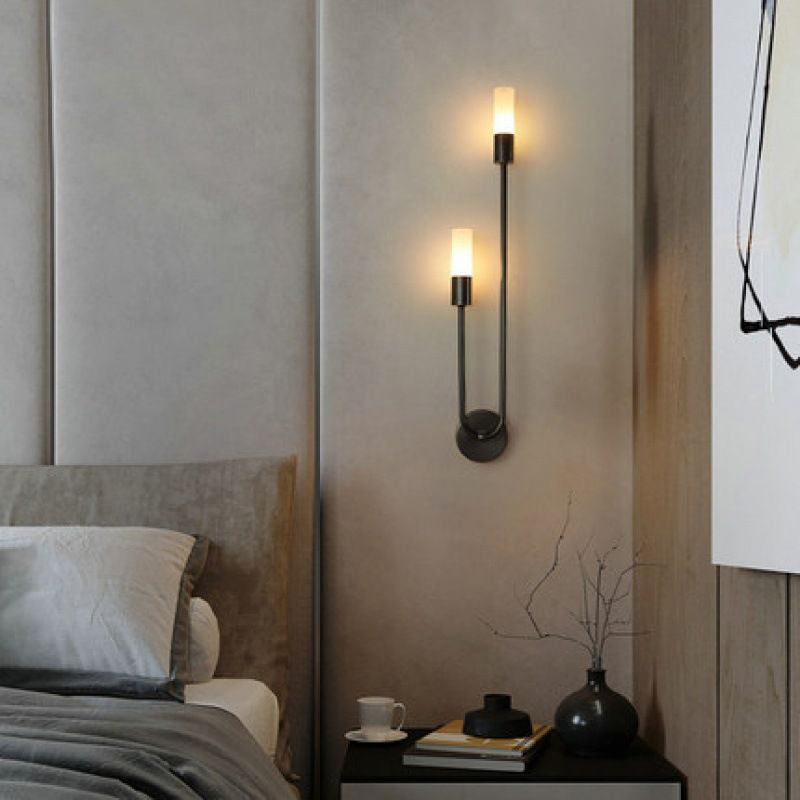 A contemporary bedroom showcases a soft gray headboard, neatly arranged pillows, and a small round table adorned with a cup and book. On the wall, XCEPTION's Nordic stick on wall lights featuring energy-saving LED technology emit warm illumination. A minimalist painting is partially visible in the background.