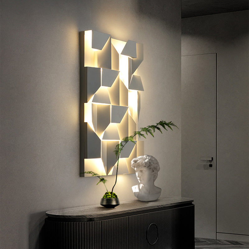 The Geometric modern wall lights by XCEPTION, featuring geometric patterns and adjustable color temperatures, cast a warm glow in a dim room. Below them, a bust sculpture and a small potted plant adorn a dark console table. A closed door is visible in the background.