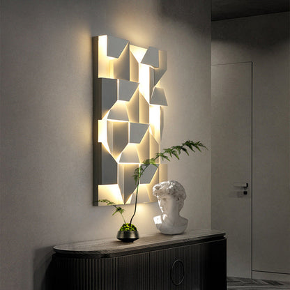 The Geometric modern wall lights by XCEPTION, featuring geometric patterns and adjustable color temperatures, cast a warm glow in a dim room. Below them, a bust sculpture and a small potted plant adorn a dark console table. A closed door is visible in the background.