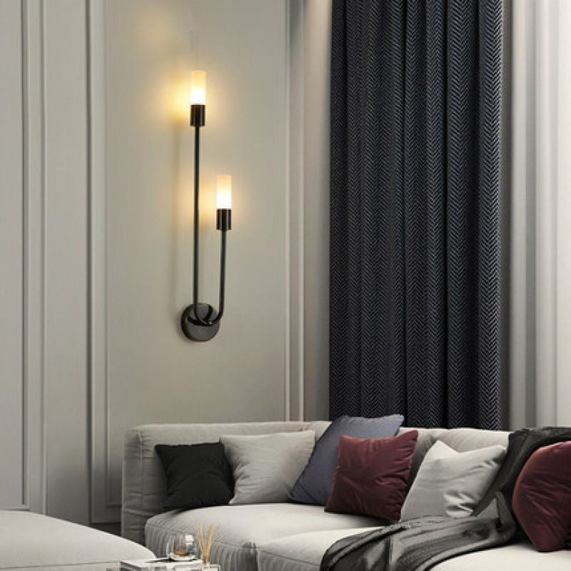A modern living room features a gray sofa adorned with multi-colored cushions. Above, two sleek XCEPTION Nordic stick on wall lights provide warm illumination on the light gray wall. To the right, dark patterned curtains contribute to a stylishly cozy ambiance.