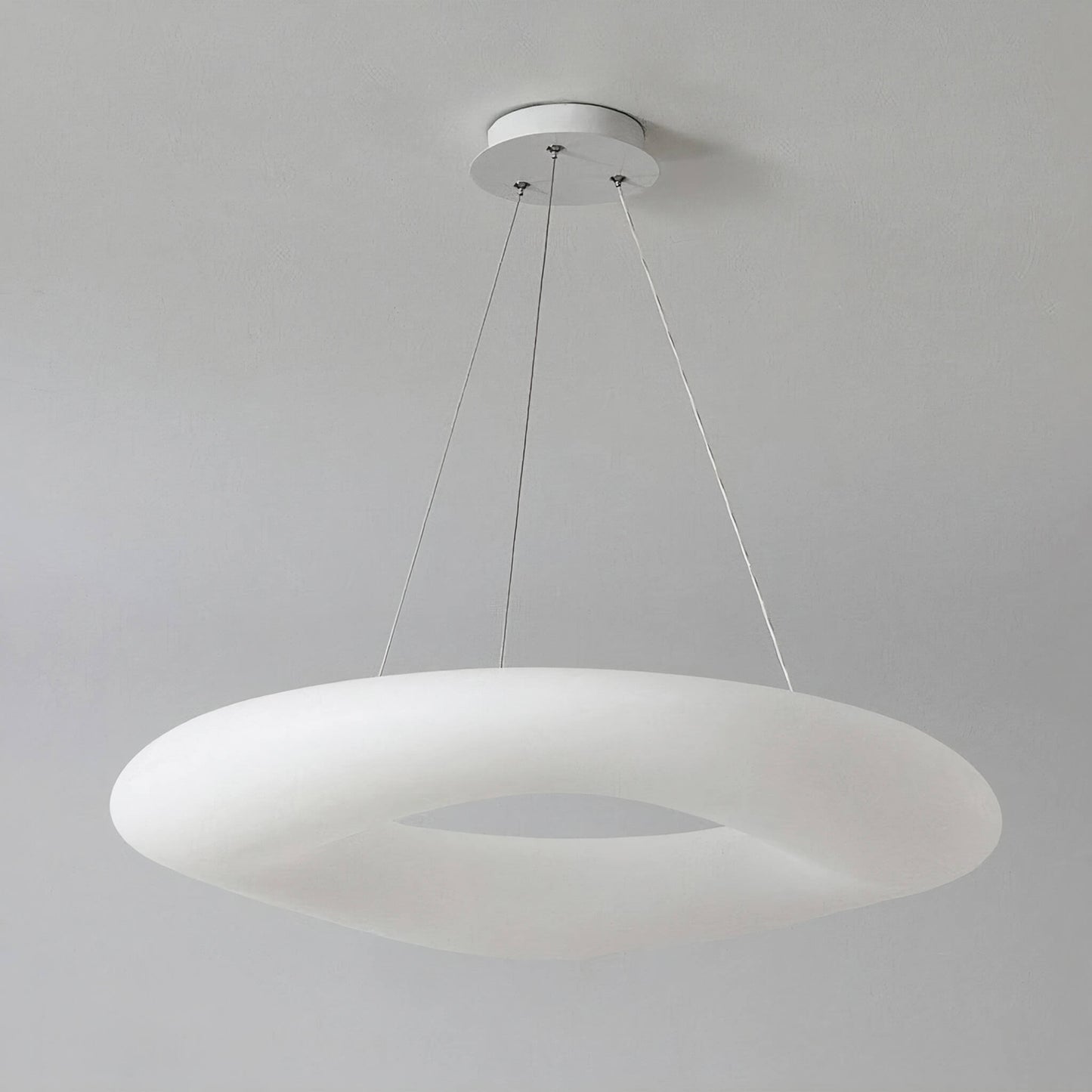 The Cloud Ceiling Light by XCEPTION is a contemporary white, doughnut-shaped pendant fixture hung from the ceiling with three slender wires, offering a minimalist and elegant appearance against a simple gray background.