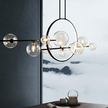 Hanging in front of a large window is the Comos Ceiling Light by XCEPTION, featuring spherical glass bulbs and a circular metal frame. Outside, you can see fog-covered mountains, while below, a tea set rests on a wooden table.
