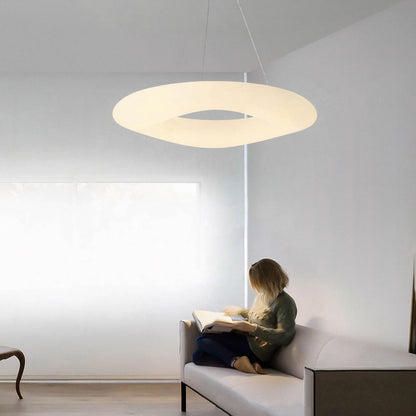 A person sitting on a gray couch, reading a book in a minimalist room, is illuminated by the large Cloud Ceiling Light from XCEPTION hanging above them. The neutral walls and decor contribute to a calm and serene atmosphere.